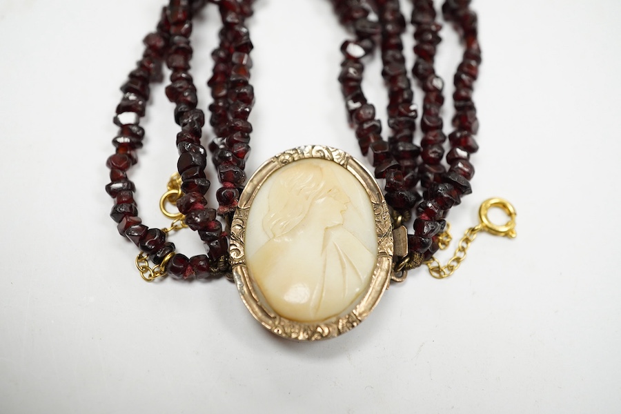 A late 19th/early 20th century multi strand rough cut garnet set necklace, with a yellow metal mounted oval cameo shell clasp, 43cm. Condition - poor to fair